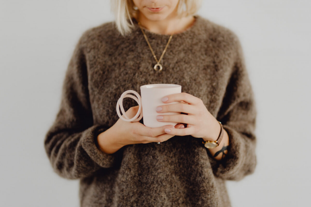 セーターを着た女性がコーヒーカップを持っている様子